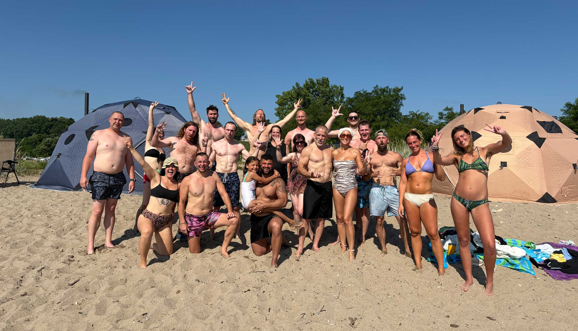 A large group of Hive participants gathered on the beach between two sauna tents